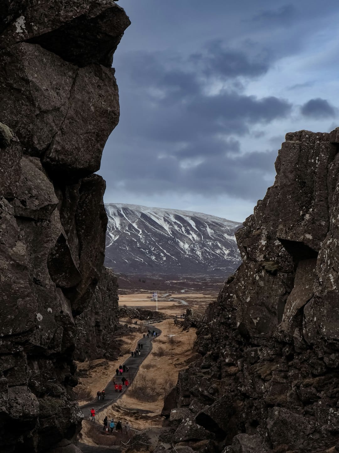 Tourists walk a path through a rocky gorge with mountains beyond.